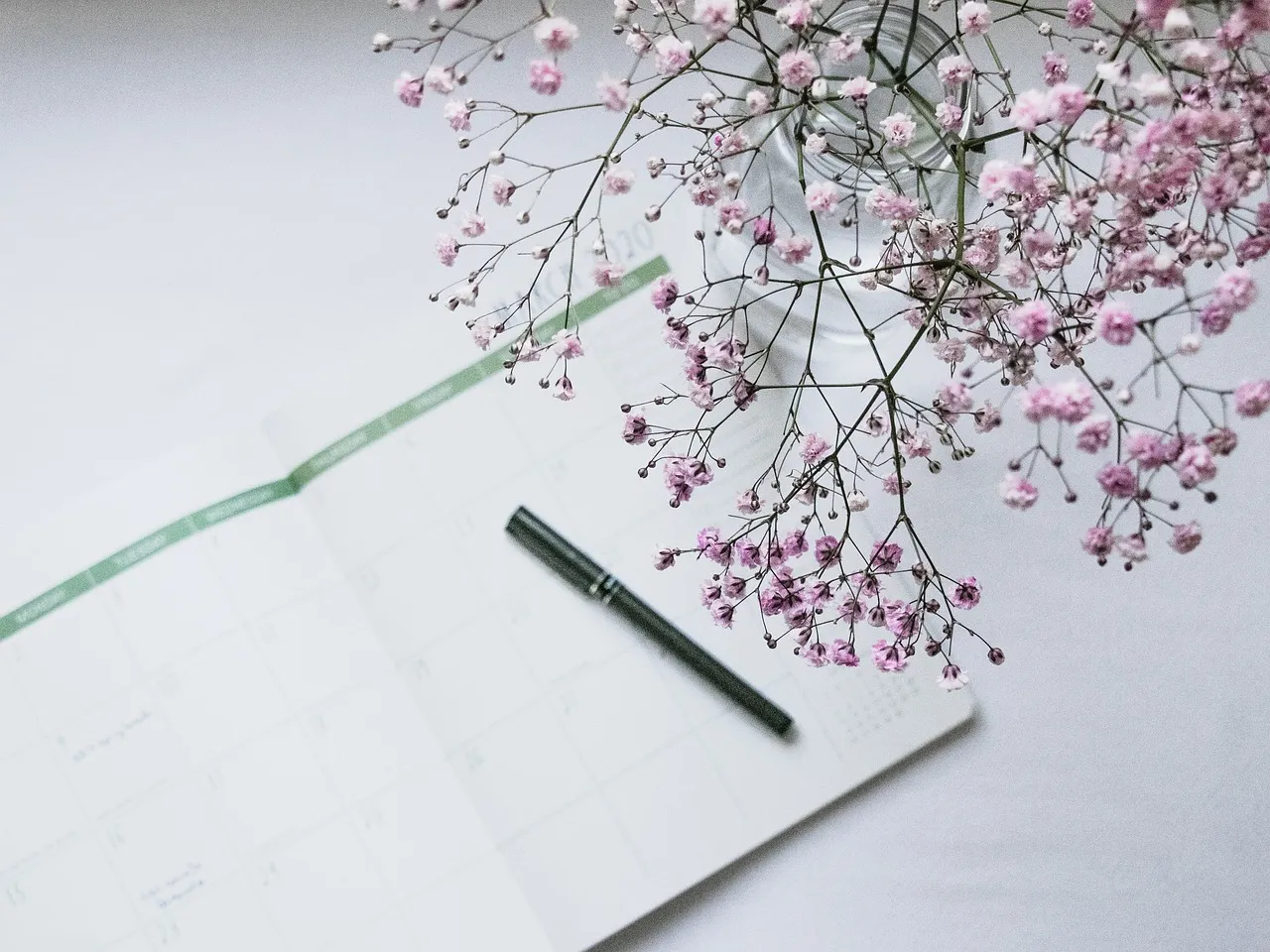 Aufgeschlagener Monatskalender mit Stift und Blüten