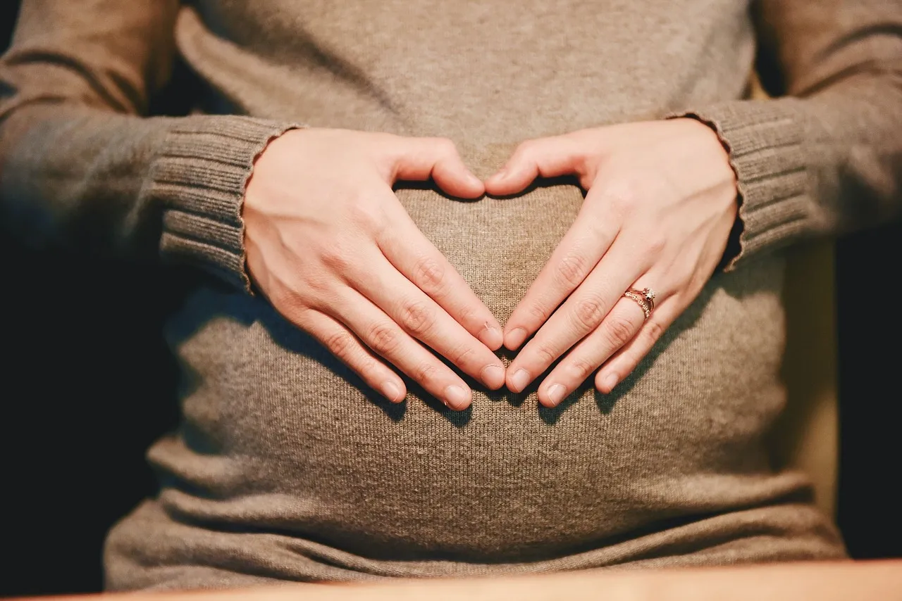 Schwangere formt mit den Händen ein Herz auf dem Bauch